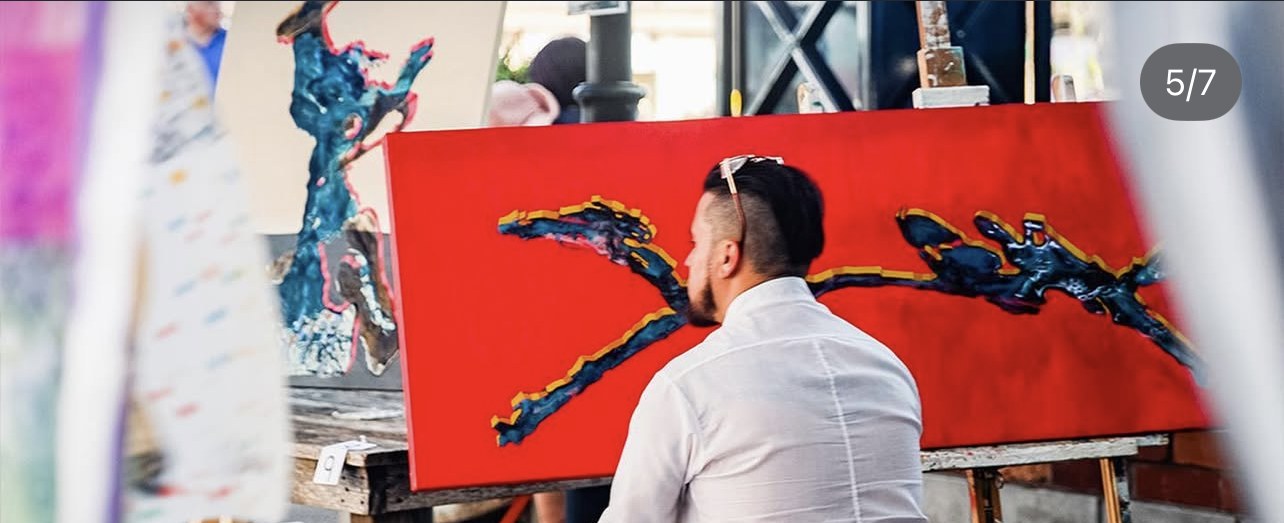 Artist with red canvas painting in progress.