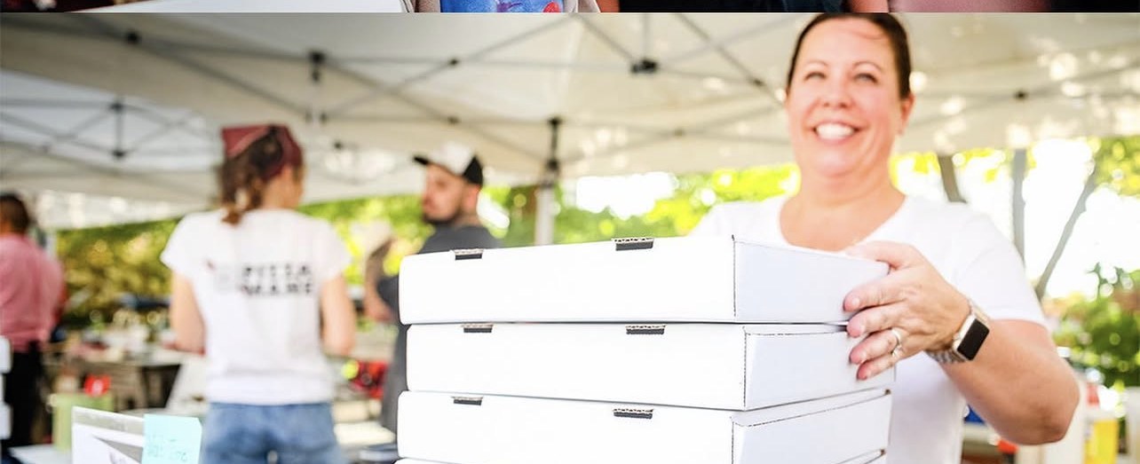 Smiling pizza vendor with stack of boxes.